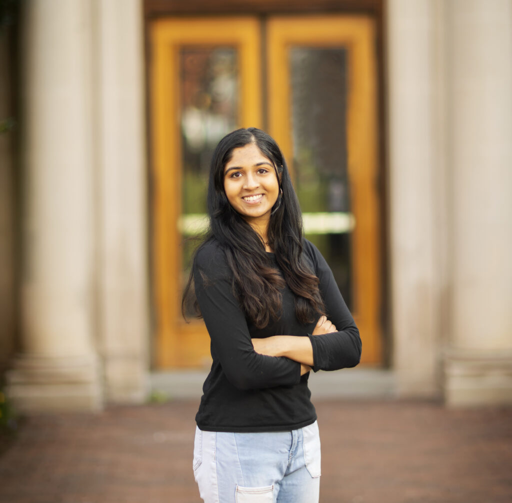 A portrait of Aashika Vishwanath with her arms crossed in front of Towne Hall. 