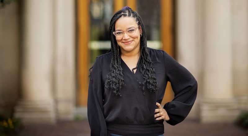Ro Encarnación, a doctoral student at Penn Engineering, smiles at the camera while wearing a black long-sleeve blouse and her hair in braids. 