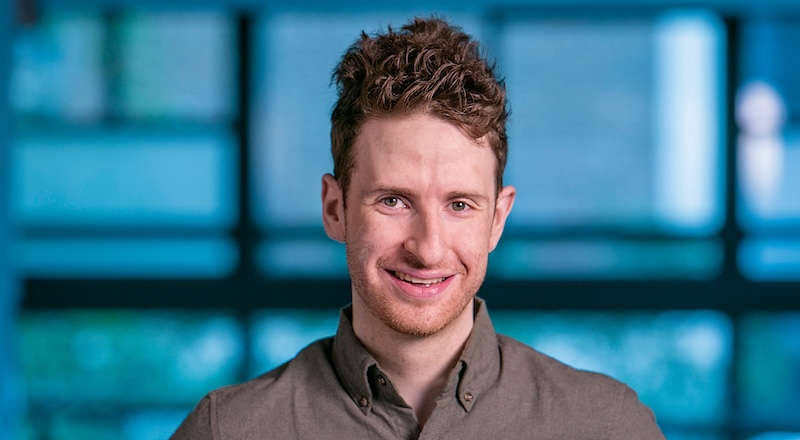 Jacob Gardner smiles at the camera while wearing a button-down shirt