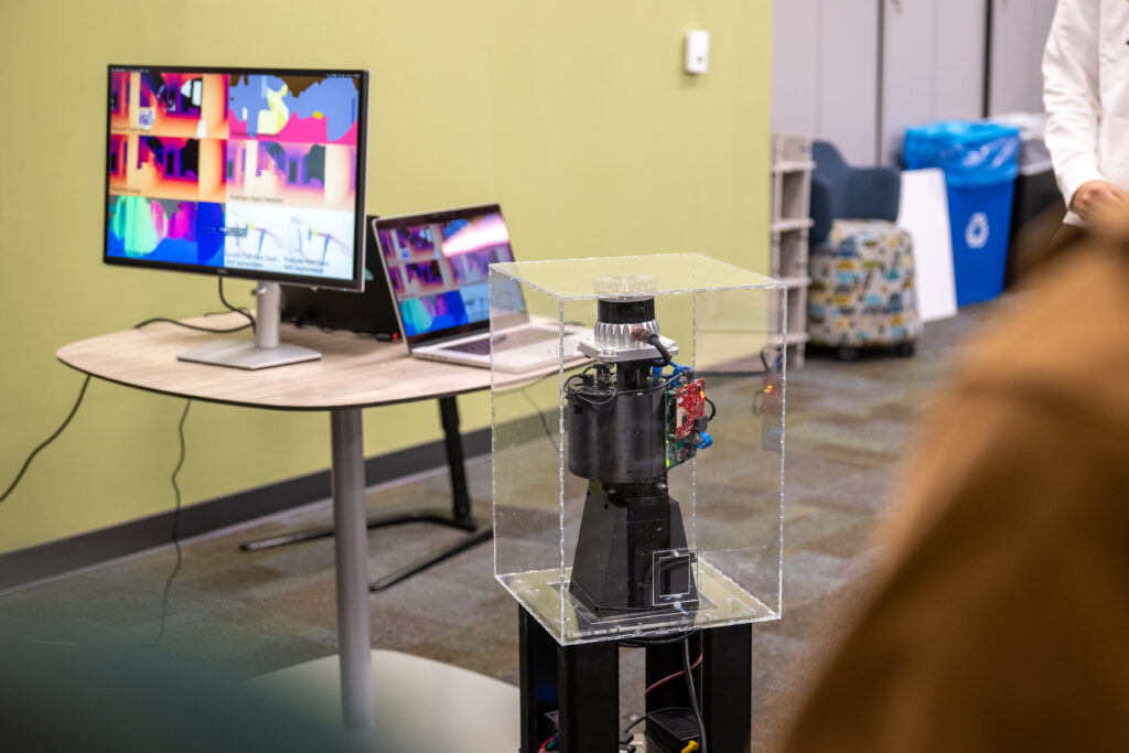 A columnar robot stands next a computer showing what the robot sees.