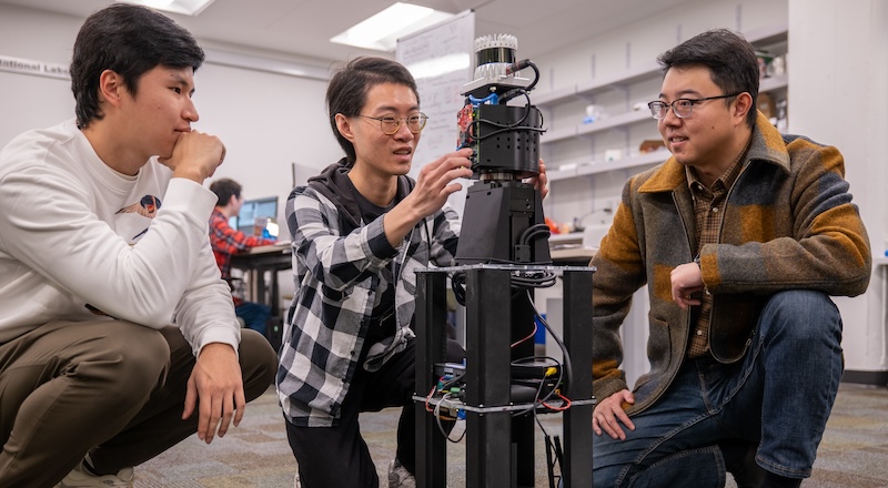 Three researchers squat near a robot.